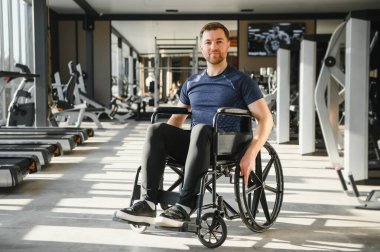 Tekerlekli sandalye kullanan bir adamın portresi, spor salonunda çalışmaktan zevk alıyor, fiziksel kısıtlamalara rağmen dahil olmayı ve aktif bir yaşam tarzını teşvik ediyor.