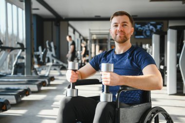 Engelli bir adam modern spor salonunda tekerlekli sandalyede egzersiz yapıyor, rehabilitasyon görüyor ve spor müsabakaları düzenliyor.