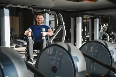 Tekerlekli sandalyedeki gülümseyen adam modern bir spor salonunda rehabilitasyon sırasında ağırlık kaldırıyor.
