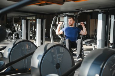 Dambıllarla egzersiz yapan, ulaşılabilir spor salonunda rehabilitasyon sırasında esneklik ve güç sergileyen kişi.