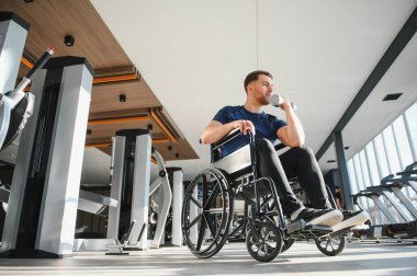 Modern spor salonunda ağırlıklarla egzersiz yapan engelli bir adam spor yaparak kapsayıcılığını ve rehabilitasyonunu gösteriyor.