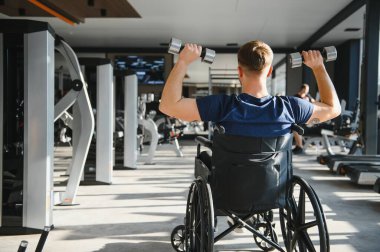 Hasta rehabilitasyon merkezinde fizyoterapi seansı sırasında halterlerle egzersiz yapıyor, sakatlıktan sonra güç ve hareket kabiliyetini artırıyor.