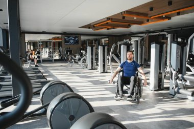 Dambıl kullanan engelli biri, rehabilitasyon ve kapsayıcı fitness için donanımlı bir spor salonunda çalışıyor.