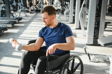 Tekerlekli sandalyedeki dambıllarla egzersiz yapan engelli bir kişi, fitness merkezinde dayanıklılık ve kararlılık gösteriyor