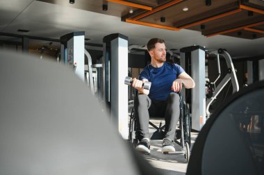 Modern spor salonunda dambıllarla egzersiz yapan, rehabilitasyona giden ve adapte olmuş egzersizler yaparak direnç gösteren bir adam.