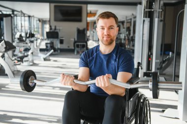 Tekerlekli sandalyede otururken ağırlık kaldıran, spor salonunda egzersiz yapan, rehabilitasyon sırasında direnç ve güç gösteren bir adam.