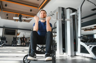 Engelli bir adam, tekerlekli sandalyede otururken ağırlık kaldıran bir sporcu, modern spor salonunda egzersiz ve rehabilitasyon için antrenman yapıyor.