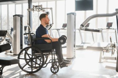 Parlak bir spor salonunda dambıllarla egzersiz yapan engelli kişi rehabilitasyon sırasında azim ve güç gösterisi yapıyor.