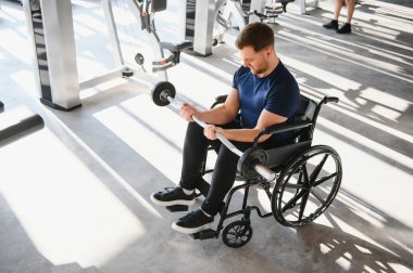 Tekerlekli sandalyedeki güçlü adam spor salonunda ağırlık kaldırıyor, rehabilitasyon ve fizik tedavi için egzersiz yapıyor, kararlılık gösteriyor ve zorlukların üstesinden geliyor.