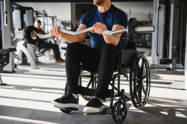Tekerlekli sandalyede otururken ağırlık kaldıran, spor salonunda egzersiz yapan, rehabilitasyon sırasında güç ve direnç gösteren erkek sporcu.