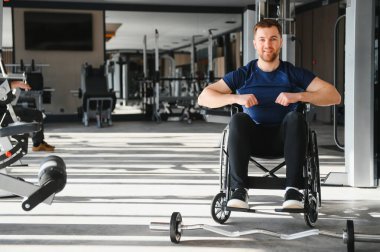 Spor salonundaki tekerlekli sandalyede gülümseyen ve antrenman yapan mutlu engelli sporcu azim ve güç gösterisi yapıyor.