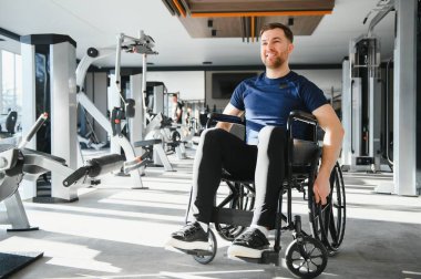 Tekerlekli sandalye kullanan gülümseyen adam ulaşılabilir bir spor salonunda çalışıyor, kararlılığını gösteriyor ve kapsayıcı uygunluğu destekliyor.