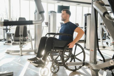 Spor salonunda tekerlekli sandalyede egzersiz yapan engelli bir adam rehabilitasyon sürecinde gücünü ve kararlılığını gösteriyor.