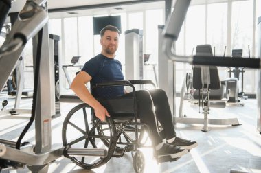 Modern bir rehabilitasyon merkezinde tekerlekli sandalyede egzersiz yapan engelli bir adam, fitness hedeflerine ulaşmak için azim ve kararlılık gösteriyor.