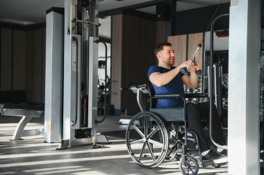Modern bir spor salonunda kablo ağırlıklarını kullanarak egzersiz yapan engelli sporcu fiziksel kısıtlamaların üstesinden gelmede kararlılık ve güç gösteriyor.
