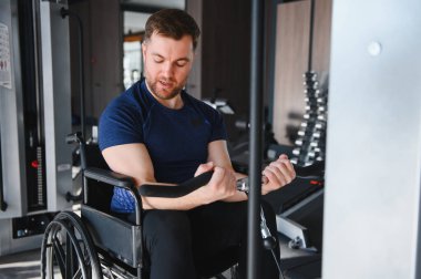 Tekerlekli sandalyedeki adam spor salonunda güç antrenmanı yapıyor, rehabilitasyona ve özel ekipmanlarla fiziksel kondisyona odaklanıyor.
