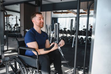 Tekerlekli sandalyedeki ağırlık makinesini kullanan gülümseyen adam, spor salonunda kaslarını çalıştıran, rehabilitasyon ve fizik tedavi için egzersiz yapan adam.