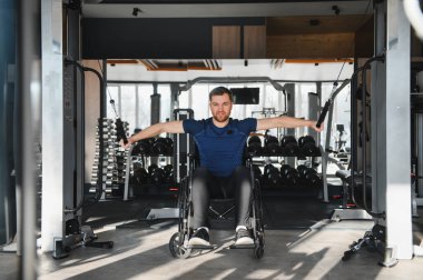 Engelli insanlar spor salonunda rehabilitasyon egzersizleri yaparlar, kablo makineleriyle üst vücut kaslarını güçlendirirler.