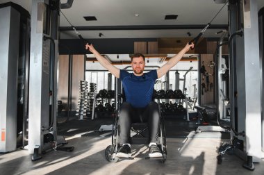 Modern bir spor salonunda kablo ağırlıklarıyla egzersiz yapan engelli biri rehabilitasyon sırasında güç, esneklik ve kararlılık gösterir.