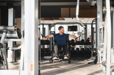 Tekerlekli sandalyedeki adam modern spor salonunda kablo ağırlığıyla egzersiz yapıyor rehabilitasyon sırasında azim ve güç gösteriyor.