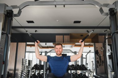 Tekerlekli sandalyede egzersiz yapan, spor salonunda kablo kullanan, rehabilitasyon sırasında azim ve güç gösteren gülümseyen adam.