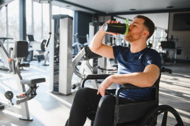 Engelli biri spor salonunda egzersiz yaptıktan sonra protein içeceği içer, sporu ve rehabilitasyonu teşvik eder.