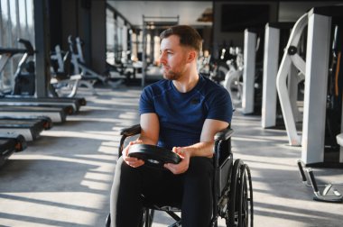 Ağırlık egzersizi yapan, modern bir spor salonunda tekerlekli sandalyede oturan, rehabilitasyon tedavisi gören ve azim gösteren beyaz tenli sporcu.