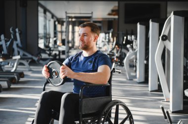 Engelli genç sporcu spor salonunda tekerlekli sandalyede egzersiz yapıyor rehabilitasyon sırasında azim ve güç gösteriyor.