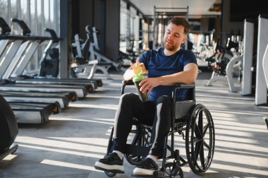 Tekerlekli sandalyedeki adam, parlak ve modern bir spor salonunda protein karışımı hazırlıyor. Spor ve rehabilitasyondaki kararlılık ve kapsayıcılık ruhunu somutlaştırıyor.