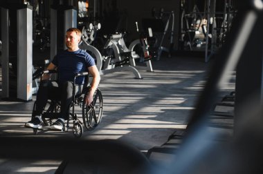 Genç adam spor salonunda tekerlekli sandalye egzersizi yapıyor, rehabilitasyon ve fizik tedavi için kapsayıcılık ve adaptasyon sporları gösteriyor.