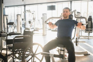 Engelli biri, rehabilitasyon için modern bir spor salonunda göğüs pres makinesi kullanıyor, kapsayıcılığı ve aktif yaşam tarzını destekliyor.