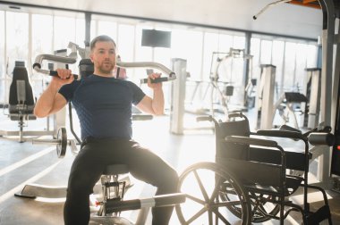 Tekerlekli sandalye kullanan bir adam spor salonunda ağırlık çalışmak, rehabilitasyon ve fizik tedavi için egzersiz yapmaktır.