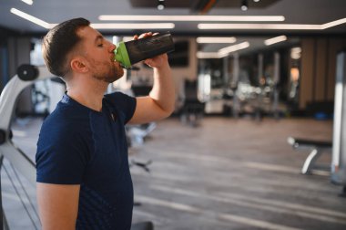 Tekerlekli sandalyedeki adam modern bir spor salonunda protein içeceği içiyor, spor rehabilitasyonunu ve engelliler için aktif yaşam tarzını vurguluyor.