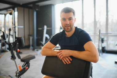 Gülümseyen adam rehabilitasyon egzersizlerini modern bir spor salonunda tamamladıktan sonra iyileşme ve refahı göstererek dinleniyor.