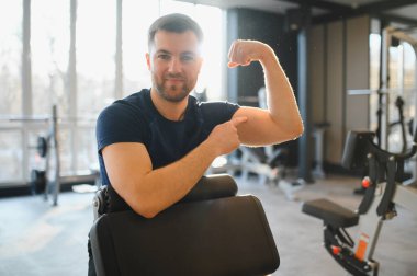 Tekerlekli sandalyedeki güçlü adam rehabilitasyon salonunda otururken kaslarını esnetiyor, fitness eğitimi sırasında azim ve gücü somutlaştırıyor.