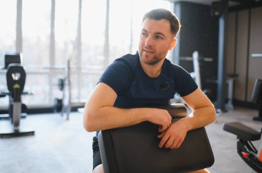 Erkek hasta, aydınlık bir spor salonunda rehabilitasyon egzersizleri yaparken dinleniyor. İyileşme ve iyileşme belirtisi gösteriyor.