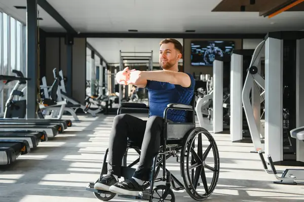 Spor salonunda tekerlekli sandalyede oturan engelli bir adam rehabilitasyon ve refah için egzersiz yapıyor.