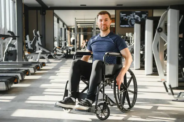 Tekerlekli sandalye kullanan bir adamın portresi, spor salonunda çalışmaktan zevk alıyor, fiziksel kısıtlamalara rağmen dahil olmayı ve aktif bir yaşam tarzını teşvik ediyor.