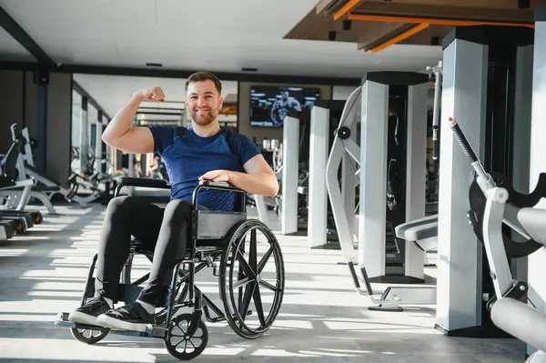 Engelli güçlü sporcu spor salonunda antrenman yapıyor, tekerlekli sandalyede oturuyor ve pazılarını gösteriyor.