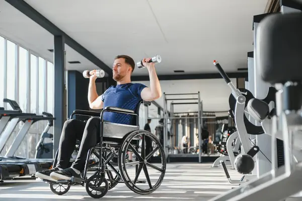 Tekerlekli sandalyedeki dambıllarla egzersiz yapan, dayanıklılık, dayanıklılık gösteren ve parlak bir spor salonu ortamında kapsayıcı spor yapmayı teşvik eden kişi.