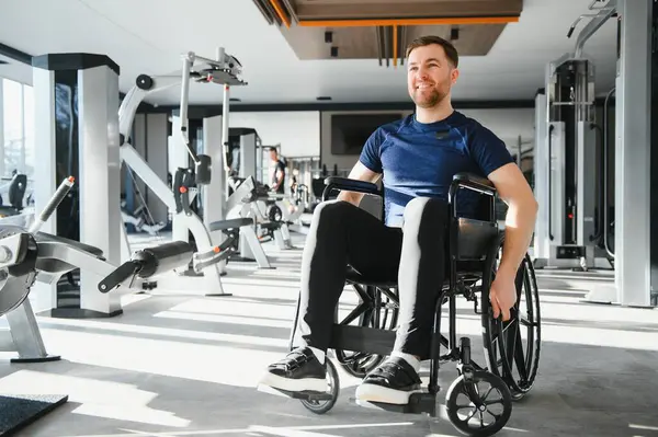 Tekerlekli sandalye kullanan gülümseyen adam ulaşılabilir bir spor salonunda çalışıyor, kararlılığını gösteriyor ve kapsayıcı uygunluğu destekliyor.