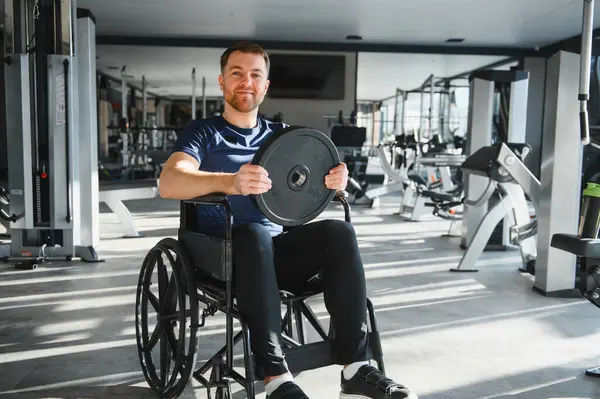 Modern spor salonunda ağırlık plakasıyla egzersiz yapan engelli bir adam spor yaparak kapsayıcılığını ve rehabilitasyonunu gösteriyor.
