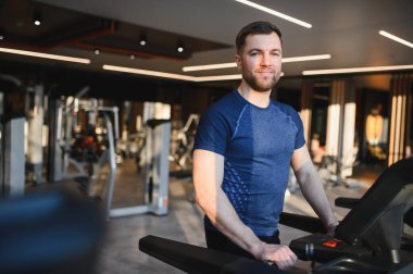 Modern bir spor salonundaki koşu bandında rehabilitasyon egzersizleri yapan sakallı bir adam aktif bir ortamda fitness ve iyileşmeye odaklanıyor.