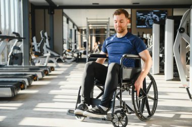 Genç adam spor salonunda tekerlekli sandalye egzersizi yapıyor. Kararlılığını gösteriyor ve sağlıklı bir yaşam tarzını adapte olmuş fiziksel aktivitelerle sürdürüyor.