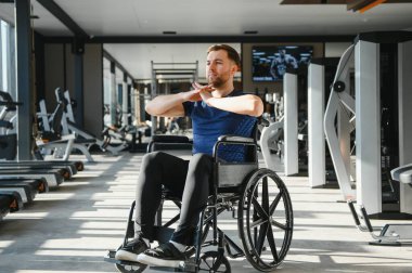 Tekerlekli sandalyedeki beyaz adam üst vücut egzersizleri yapıyor, rehabilitasyon ve adaptif sporlarda kapsayıcılık ve aktif yaşam tarzını teşvik ediyor.