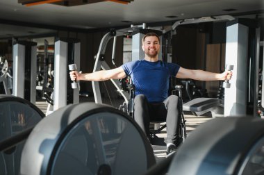 Engelli sporcu, modern bir spor salonunda tekerlekli sandalyede otururken ağırlık kaldırıyor ve kendini rehabilitasyona ve forma adadığını gösteriyor.