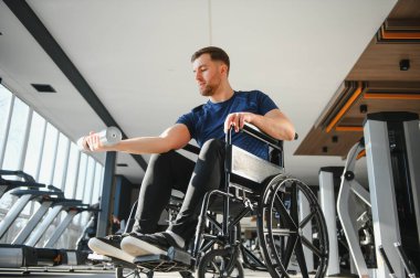 Tekerlekli sandalyedeki adam spor salonunda dambılı kaldırır, rehabilitasyona ve güç eğitimine odaklanır. Zindelik donanımlı, parlak, modern bir ortam