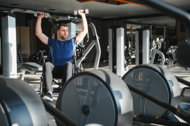 Özürlü biri, tekerlekli sandalyede ağırlık kaldıran bir sporcu, modern rehabilitasyon salonunda kollarını çalıştıran, fizik tedavi sırasında güç ve azim gösteren biri.