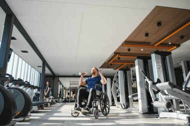 Modern spor salonunda dambıllarla egzersiz yapan engelli bir adam rehabilitasyon ve spor eğitimine bağlılığını gösteriyor.