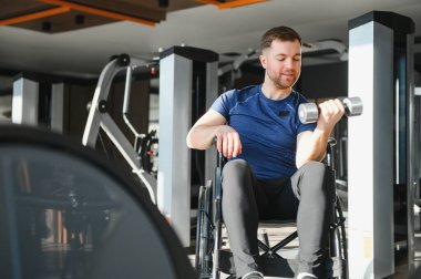 Spor salonunda ağırlık kaldıran engelli bir adam egzersiz yaparak rehabilitasyona ve iyileşmeye odaklanmış.